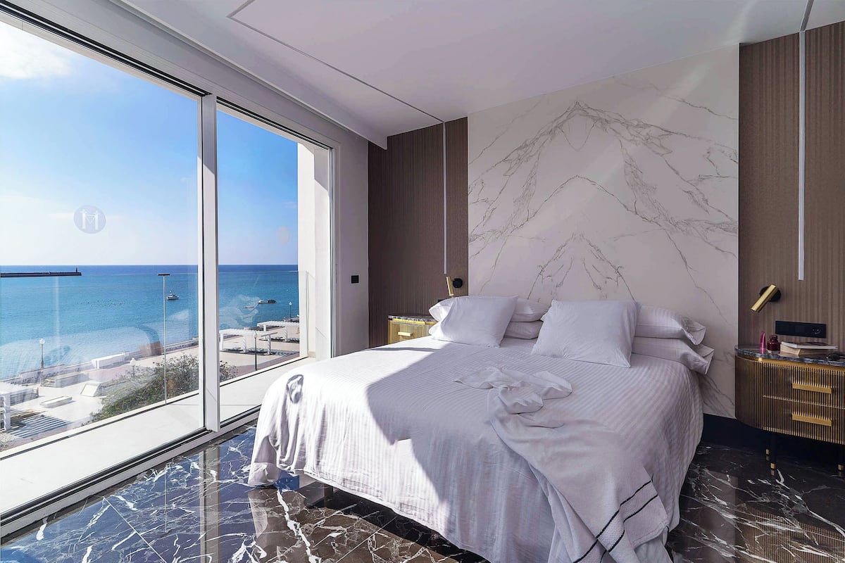 A modern bedroom with a large bed, a view of the sea, and a marble floor.
