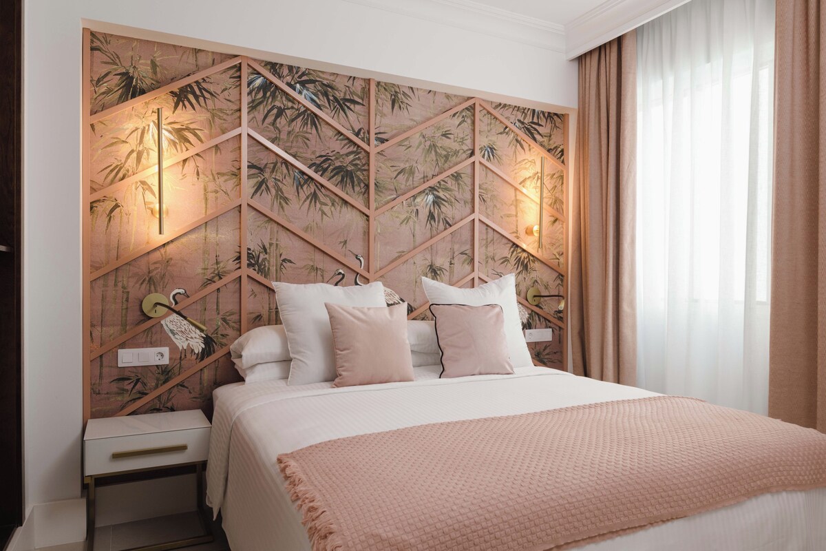 Una habitación de hotel con cama, mesita de noche, pared con motivos de bambú y ventana con cortinas.