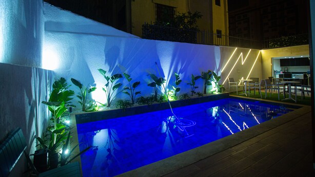 A swimming pool with plants and a neon light design, surrounded by a covered area with chairs and tables. - ABM House (Tangier)