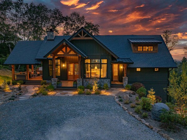 A two-story house with a stone facade, a large front porch, and a view of the ocean at sunset.