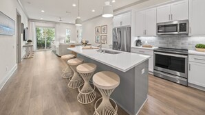 Cozinha moderna com armários brancos, eletrodomésticos de aço inoxidável, uma ilha grande com banquetas e vista para o exterior.