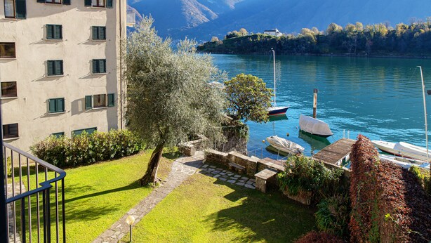 A building with a terrace overlooking a lake, boats docked, and mountains in the background. - Olea (Tremezzina)