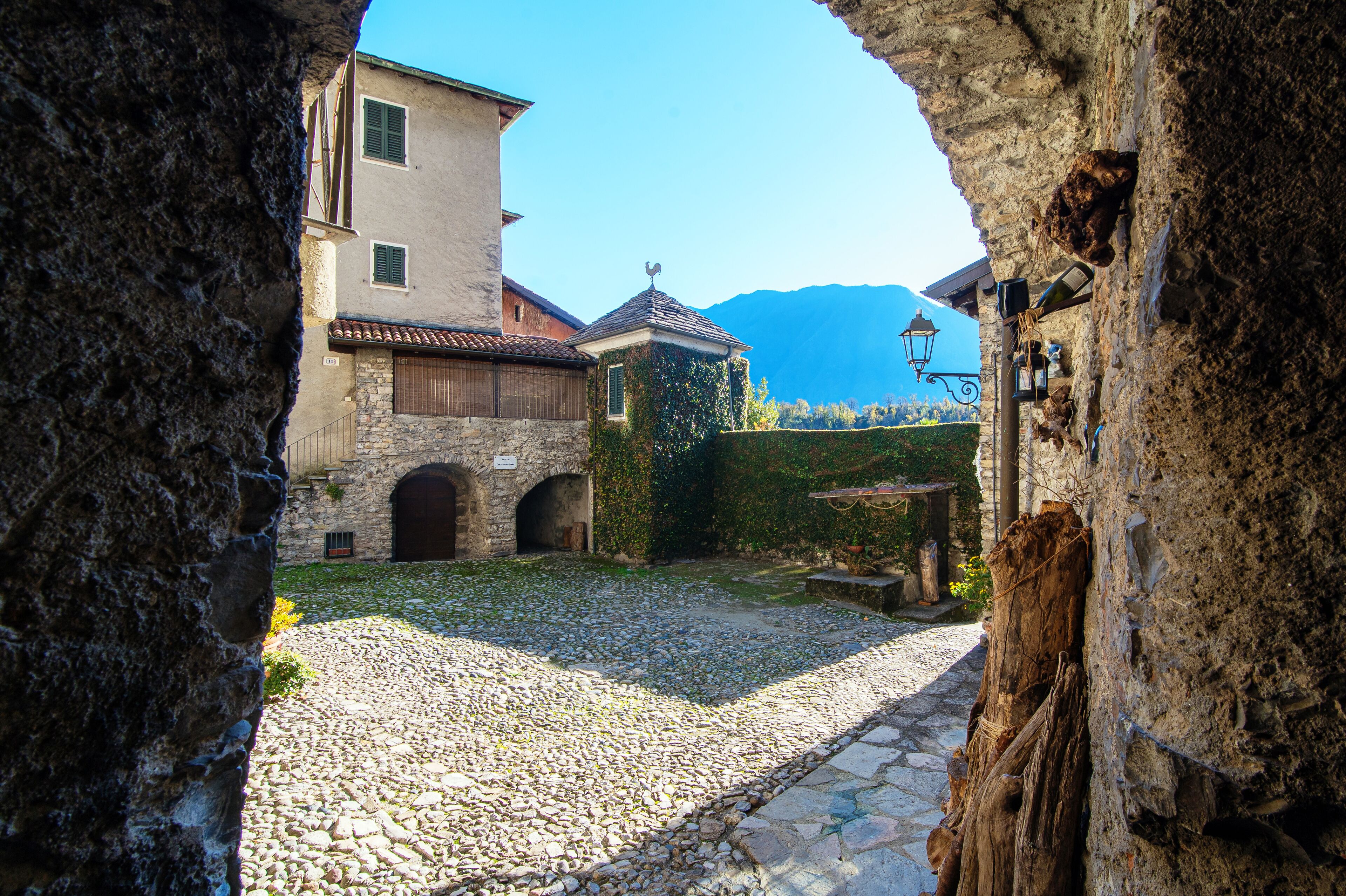 Un patio empedrado con edificios de piedra, un arco de piedra y una montaña al fondo.