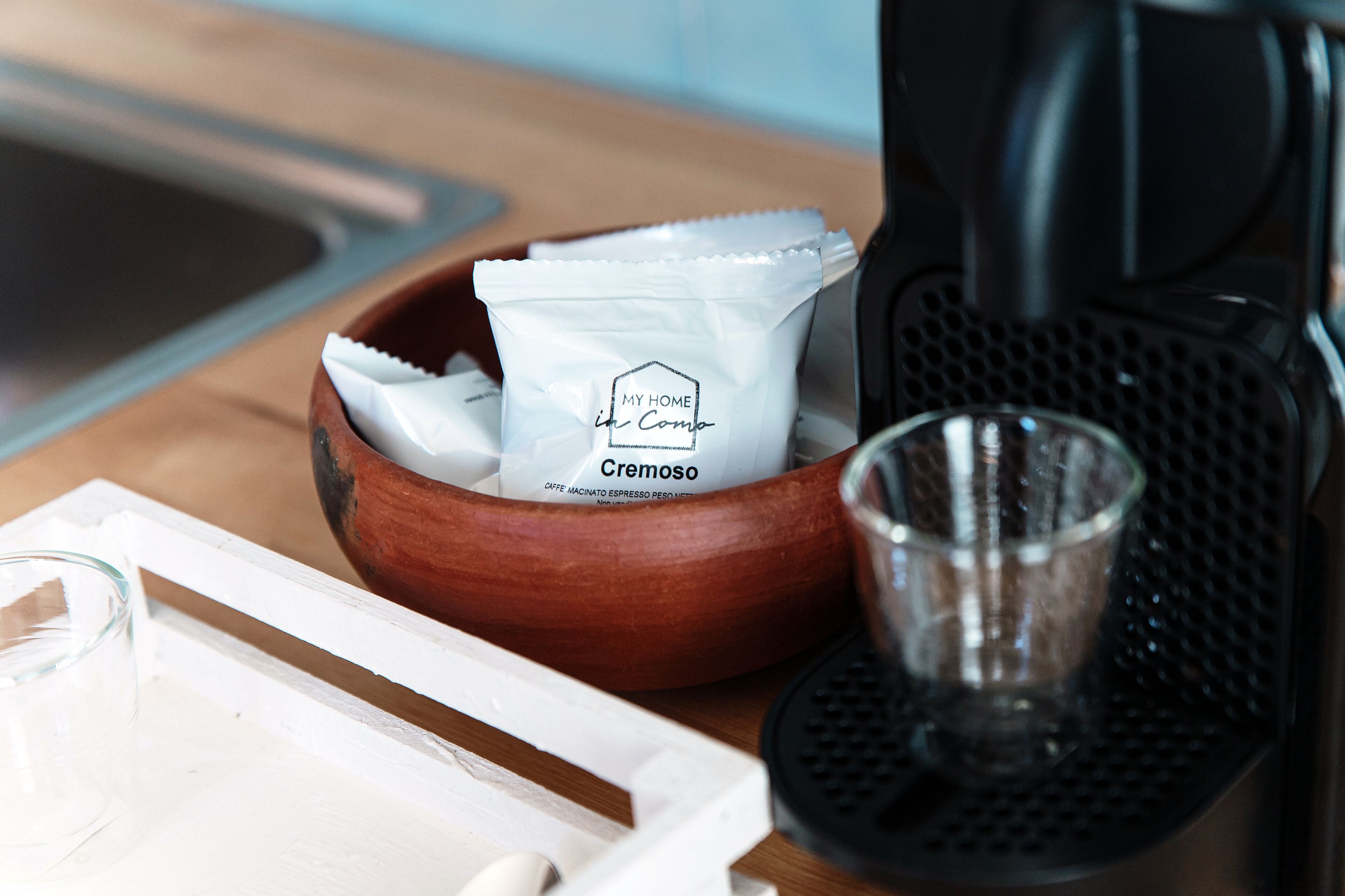 Une machine à café, un verre et un bol en bois contenant des dosettes de café, le tout posé sur un plan de travail de cuisine.