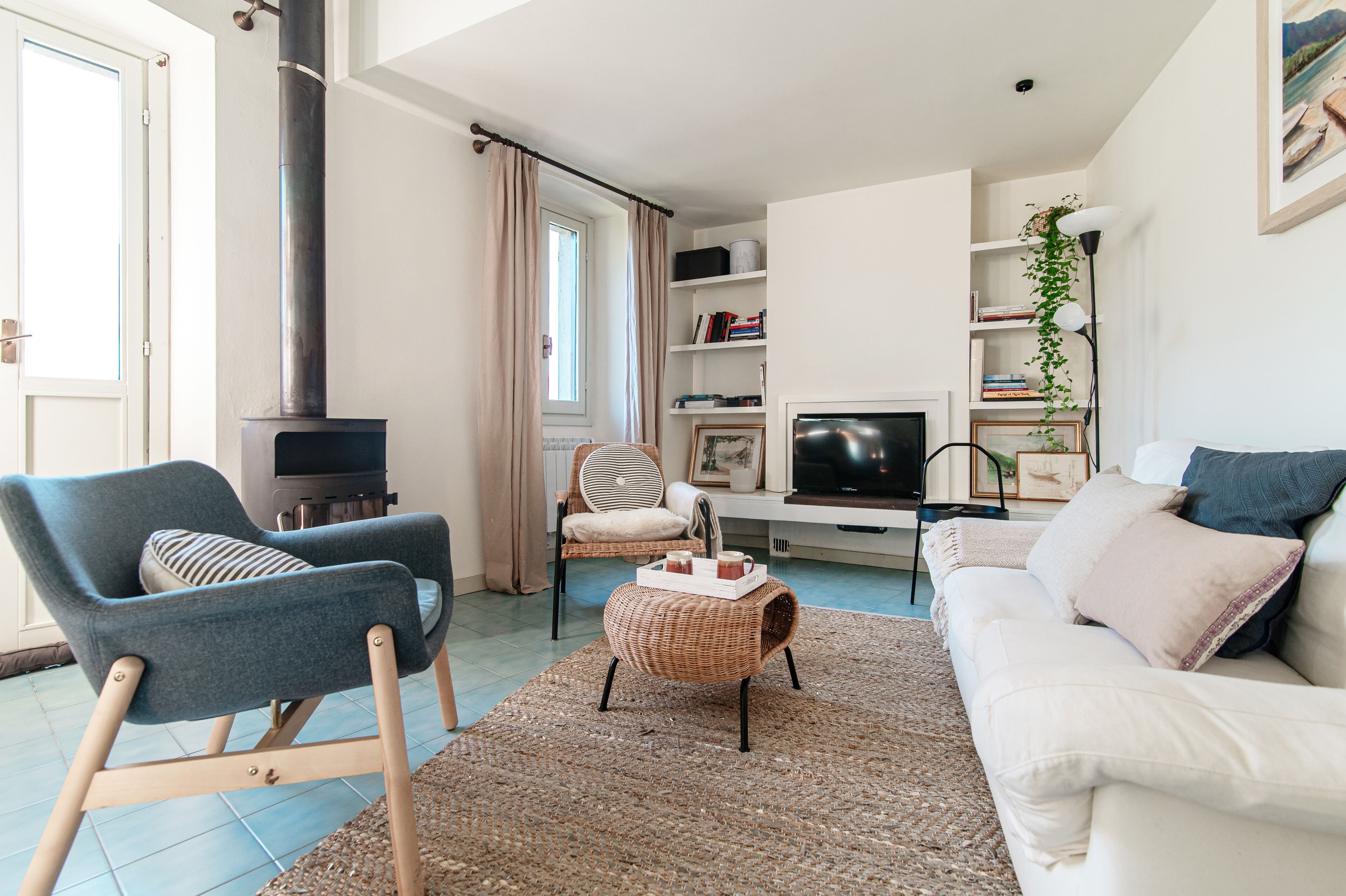 Ein Wohnzimmer mit einer Couch, einem Sessel, einem Hocker, einem Kamin, einem Fernseher und einem Bücherregal.