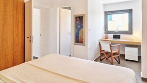 A bedroom with a bed, a desk with a laptop, a chair, and a window with natural light. - Olivea Slow Living Apartment with Pool in Chania | Alectrona Living Crete (Πλατανιάς)