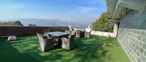 Un patio al aire libre con césped artificial, mobiliario de mimbre y vistas a montañas distantes.