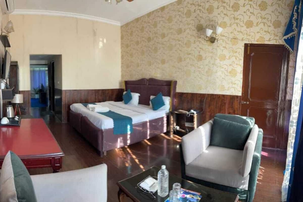 A hotel room with a bed, a desk, a chair, and a small table with a bottle and glasses.