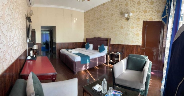 Habitación de hotel con cama, escritorio, silla y una mesita con una botella y vasos.