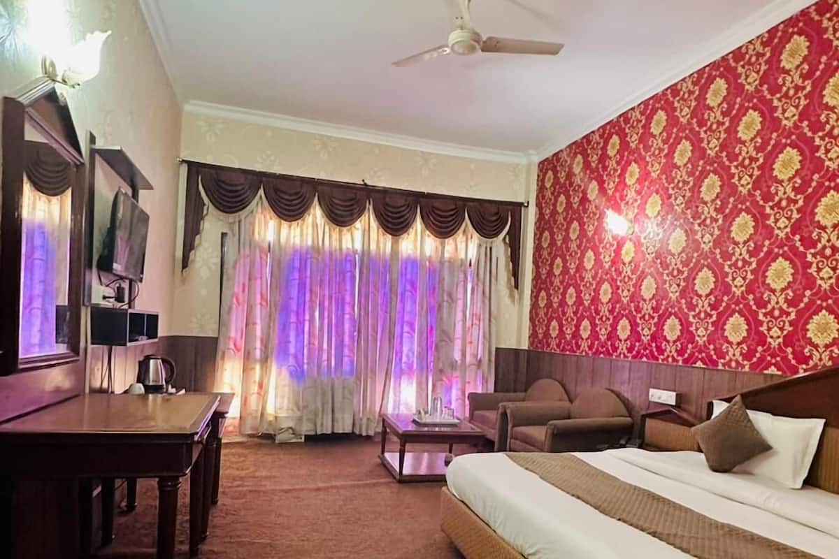 A hotel room with a bed, a sofa, a desk, a television, and curtains.
