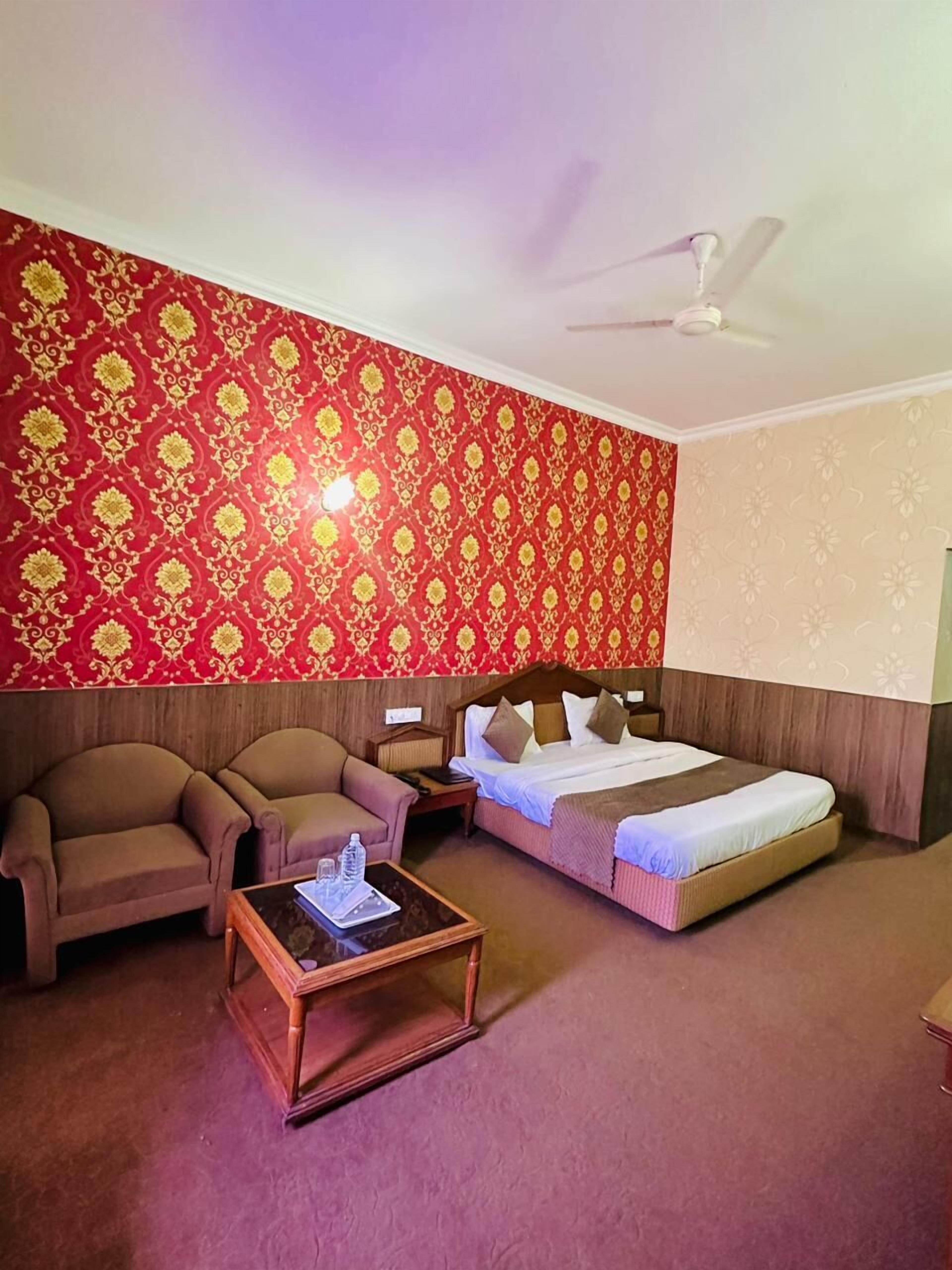 Habitación de hotel con cama, dos sillones, una mesita de madera y ventilador de techo.