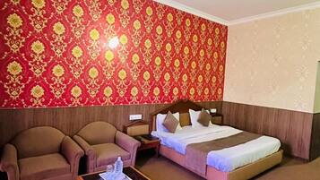 Habitación de hotel con cama, dos sillones, una mesita de madera y ventilador de techo.