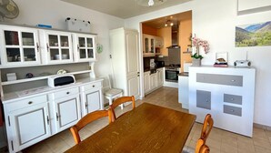 Une cuisine moderne avec des meubles blancs, une table à manger en bois et une vue sur l’espace repas.
