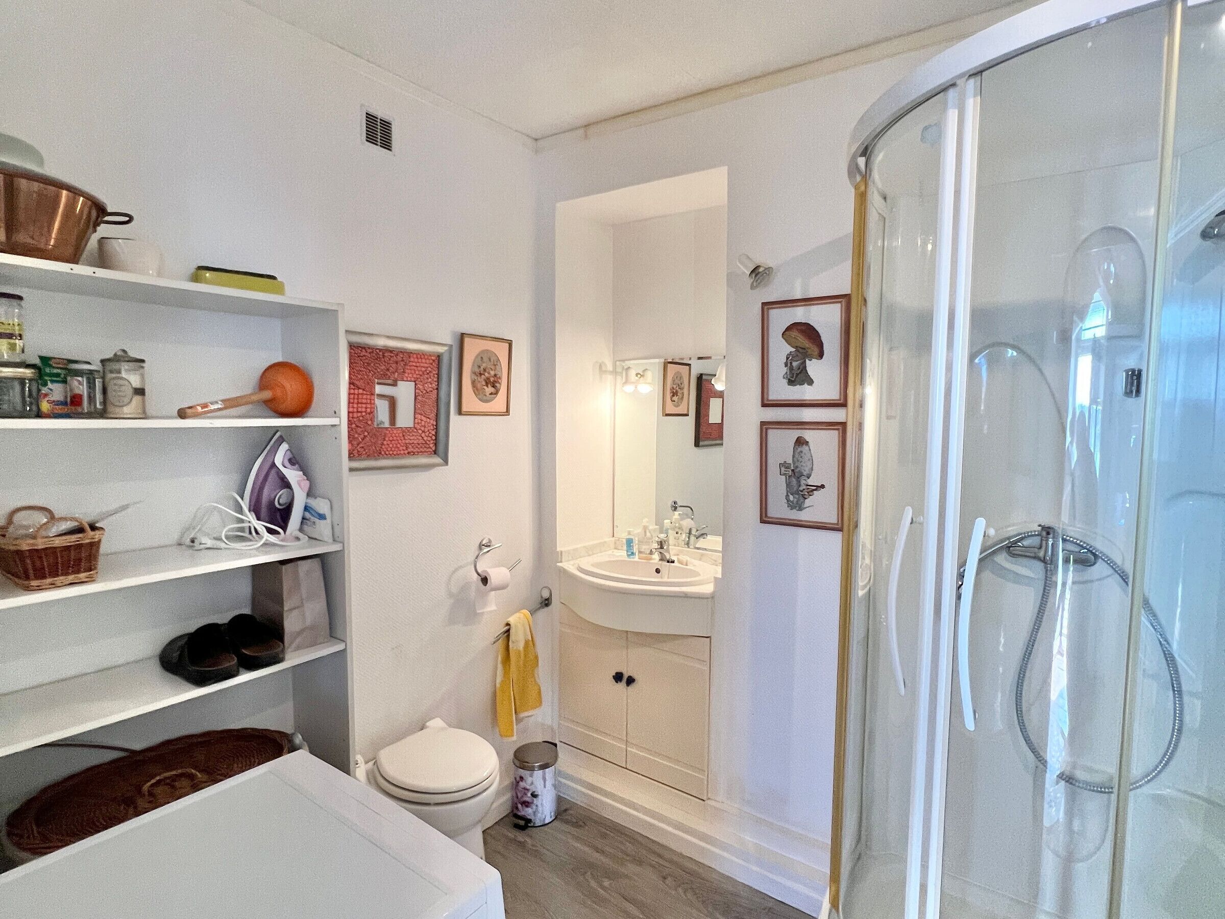 Un baño moderno con ducha, inodoro y lavamanos. Hay estantes con artículos de aseo y un espejo sobre el lavamanos.