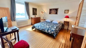 A bedroom with a bed, a desk with a laptop, a chair, a dresser, and a window with curtains.