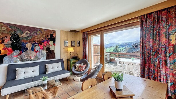 A cozy living room with a sofa, a chair, a wooden dining table, and a view of the outdoors. - Charming 2BR Apartment with Mont Blanc Views, Terrace & Parking (Demi-Quartier)