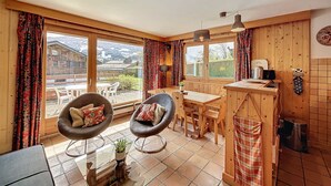 A cozy cabin with a dining area, two chairs, a wooden table, and a kitchen area with a sink and stove. - Charming 2BR Apartment with Mont Blanc Views, Terrace & Parking (Demi-Quartier)