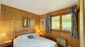 A wooden-paneled bedroom with a large bed, two bedside lamps, a window with curtains, and a radiator. - Charming 2BR Apartment with Mont Blanc Views, Terrace & Parking (Demi-Quartier)