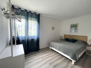 A bedroom with a bed, a bedside table, a lamp, a wall-mounted picture, and a window with curtains.