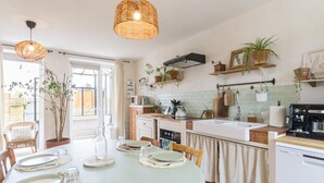 A modern kitchen with a dining area, featuring a round table set for four, a built-in oven, and a coffee machine.