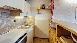 Une cuisine de taille réduite, équip ée d’une cuisinière, d’un évier et de meubles de rangement en bois.