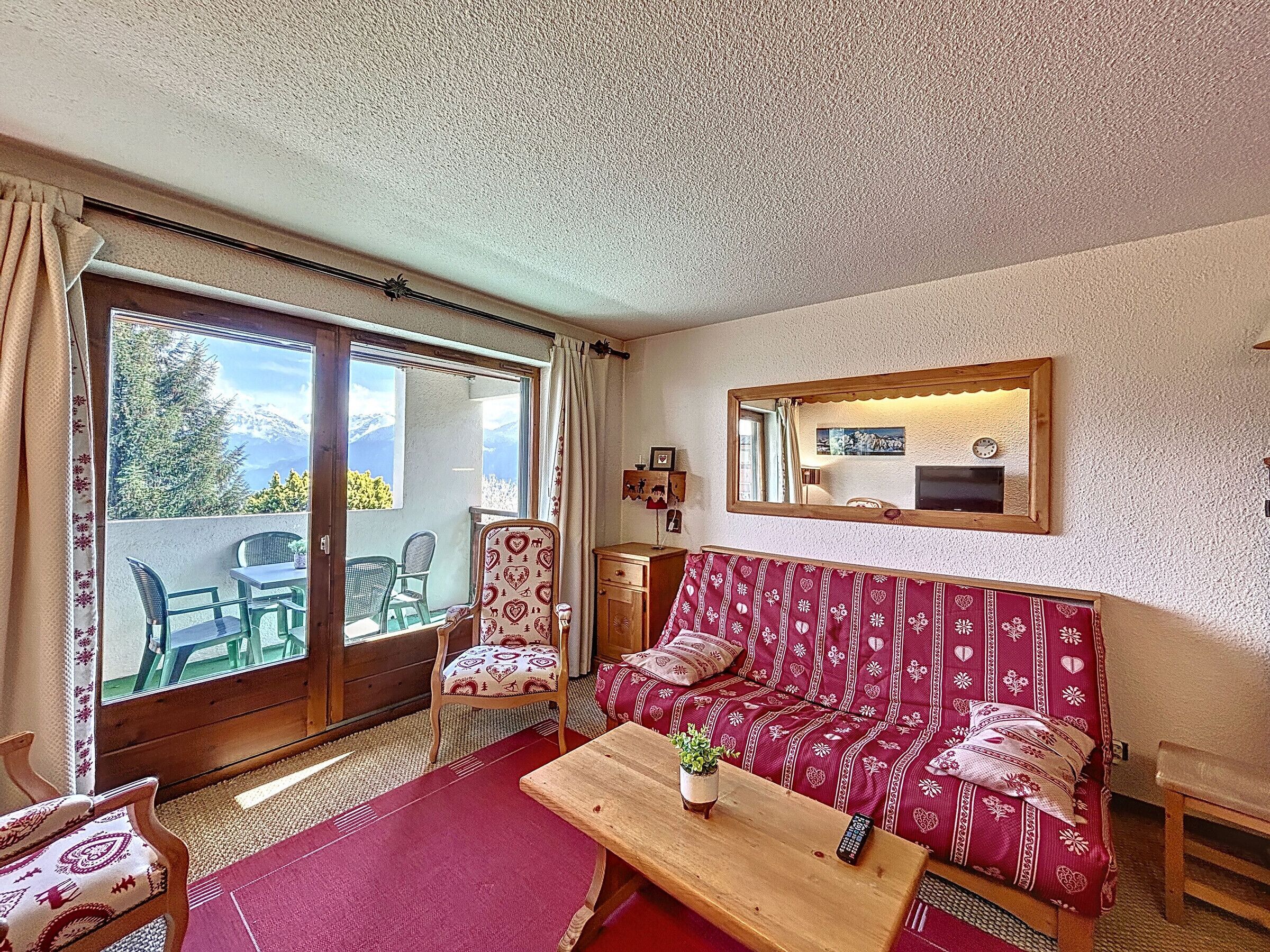A cozy living room with a sofa, chairs, a wooden coffee table, and a large window offering a mountain view.