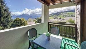 Un balcon avec une table et des chaises, une plante en pot et une vue sur un paysage montagneux.