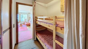 Une chambre avec des lits superposés, une porte en bois et une vue sur un espace extérieur aménagé avec une table et des chaises.
