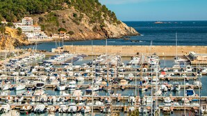 Un port esportiu amb nombroses embarcacions amarrades, un litoral rocos i edificis al fons.