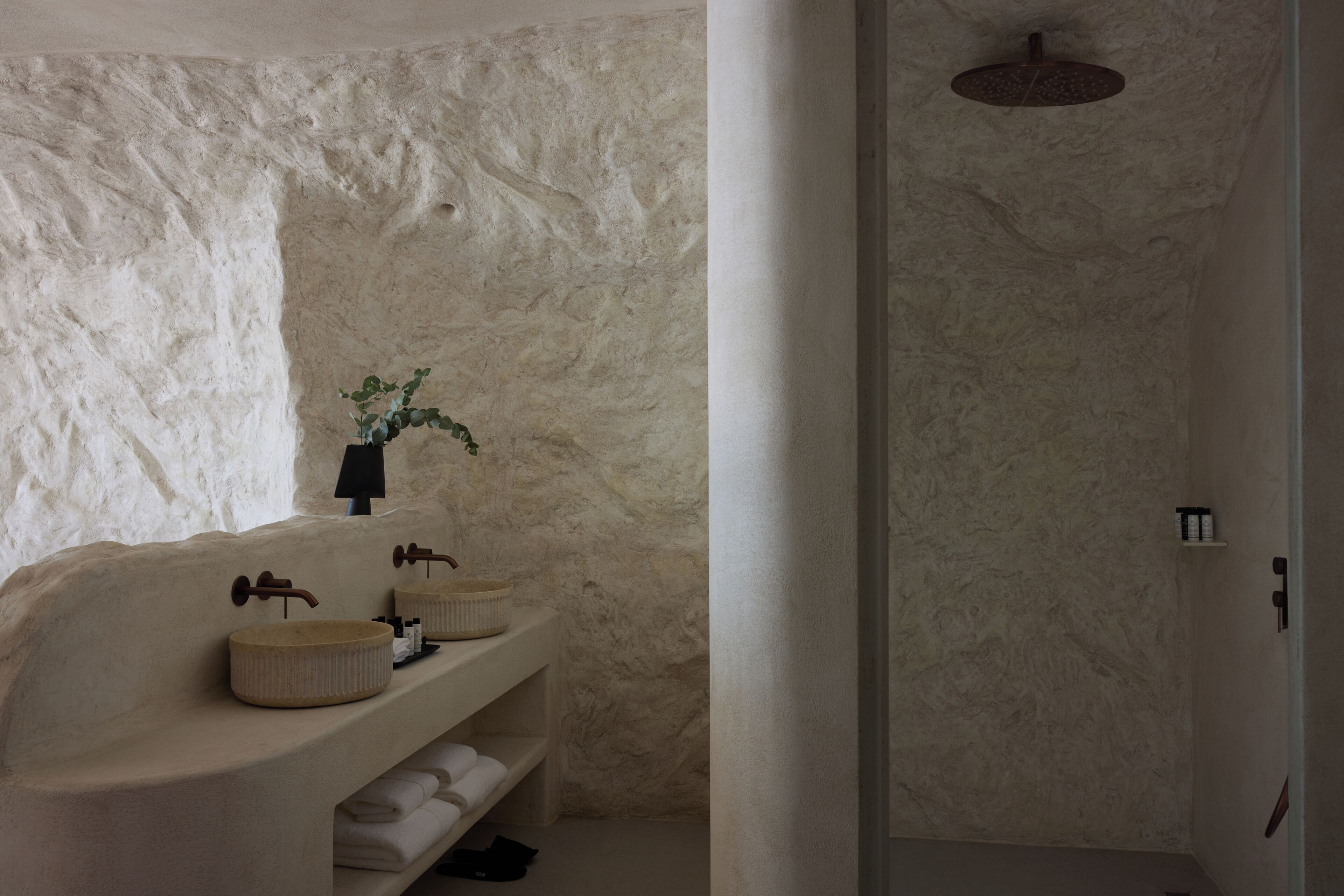 Un baño con pared de piedra, un lavamanos redondo, ducha y un perchero para toallas.