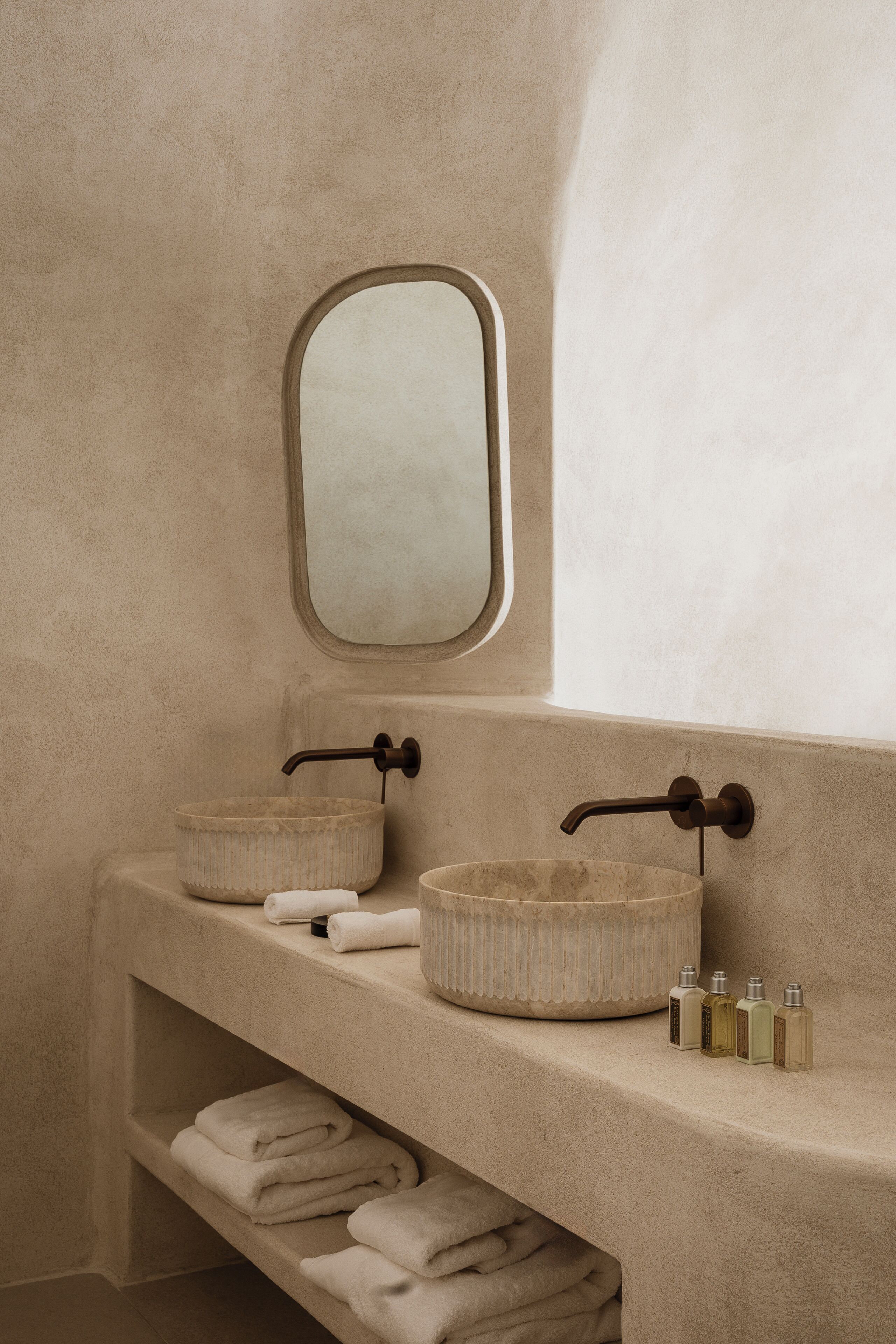 Un bagno con due lavandini, uno specchio e uno scaffale con asciugamani e articoli da toilette.