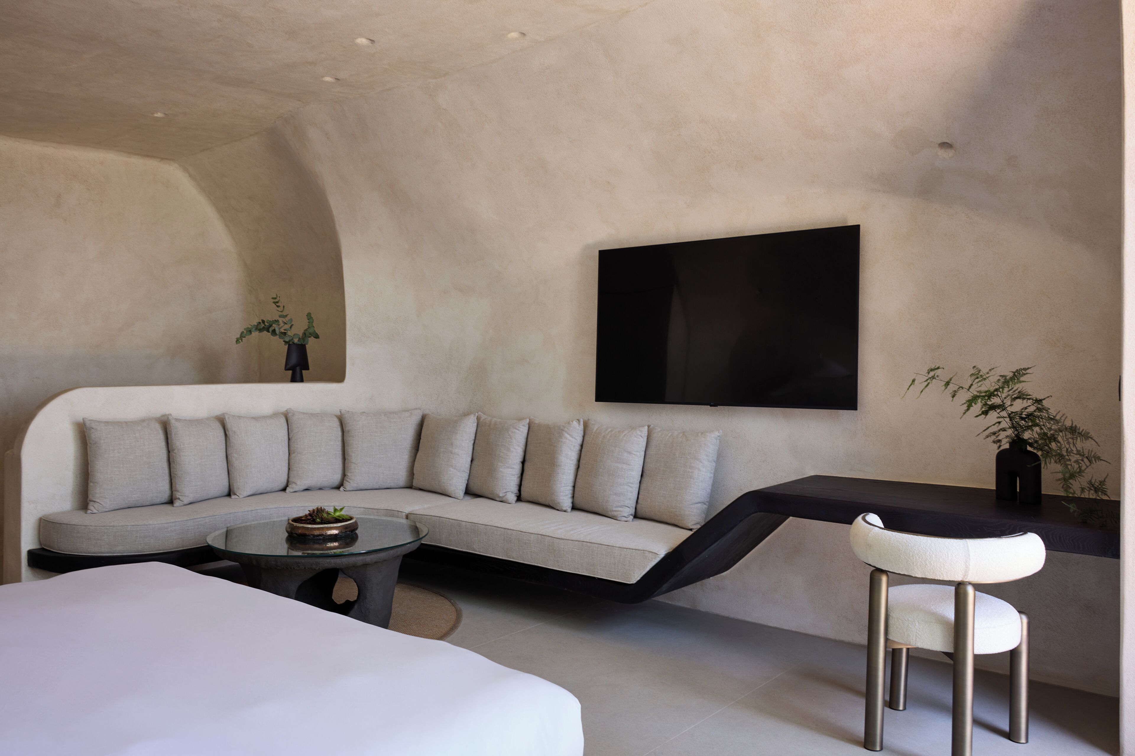 A modern living room with a curved sofa, a coffee table, a white armchair, and a flat-screen TV mounted on the wall.