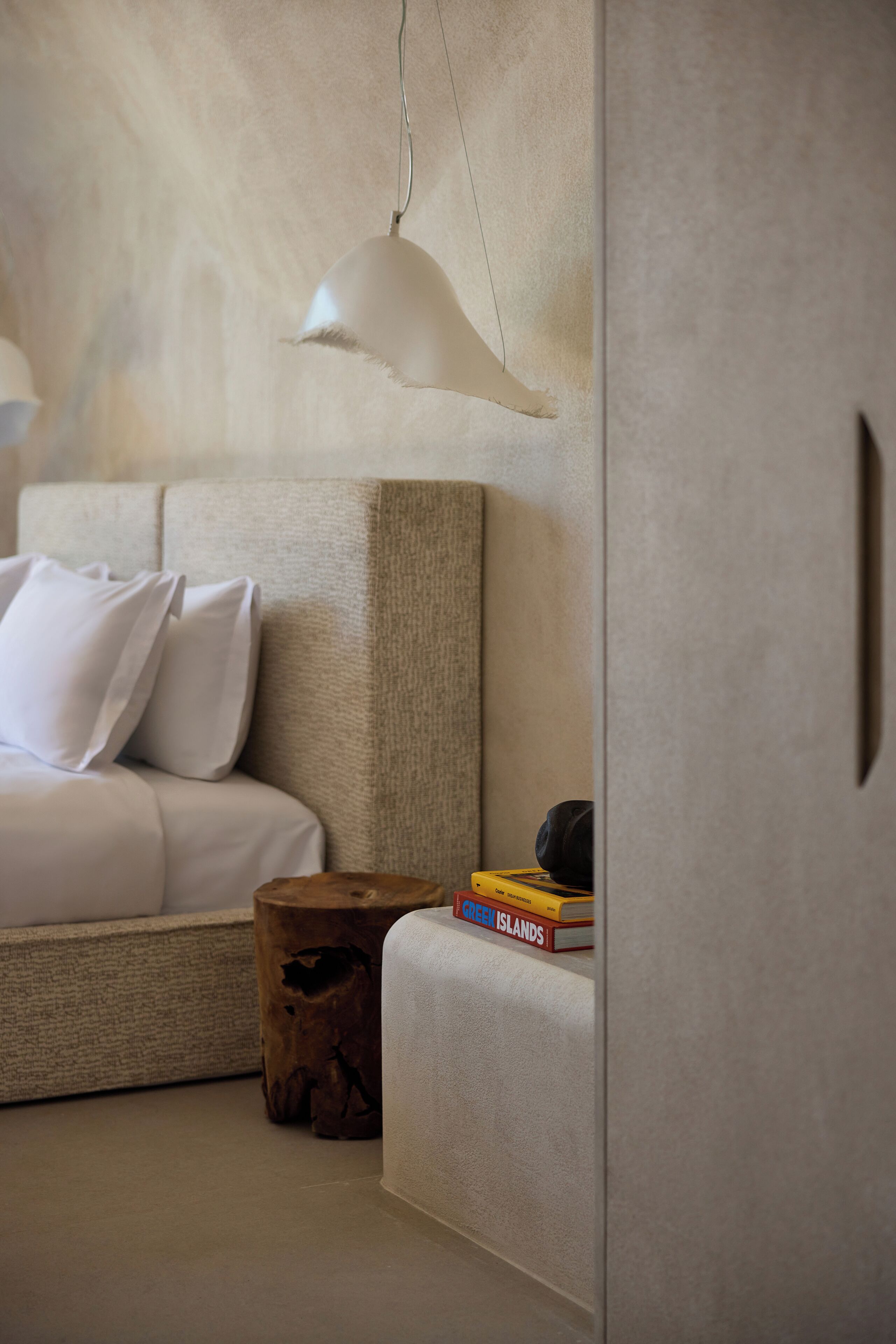 Un dormitorio moderno con una paleta de colores neutros, que incluye una cama con ropa de cama blanca, una mesita de noche de madera y una pila de libros.