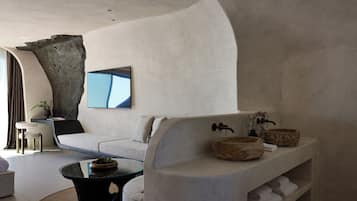 Un salón moderno con un sofá curvo, una mesa de centro de vidrio y una repisa de piedra con toallas y objetos decorativos.