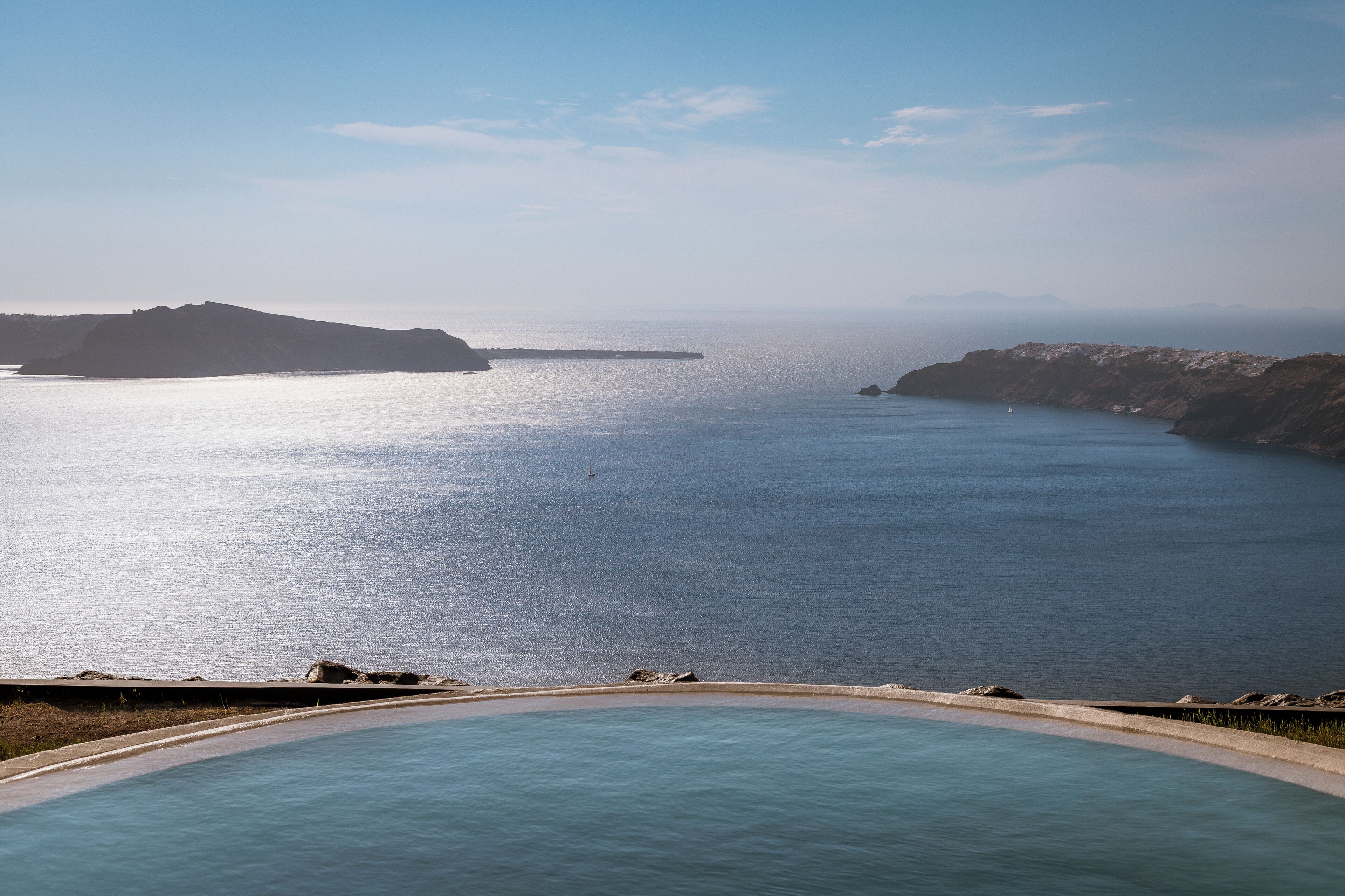 A coastal view with a swimming pool, calm sea, and distant landforms.
