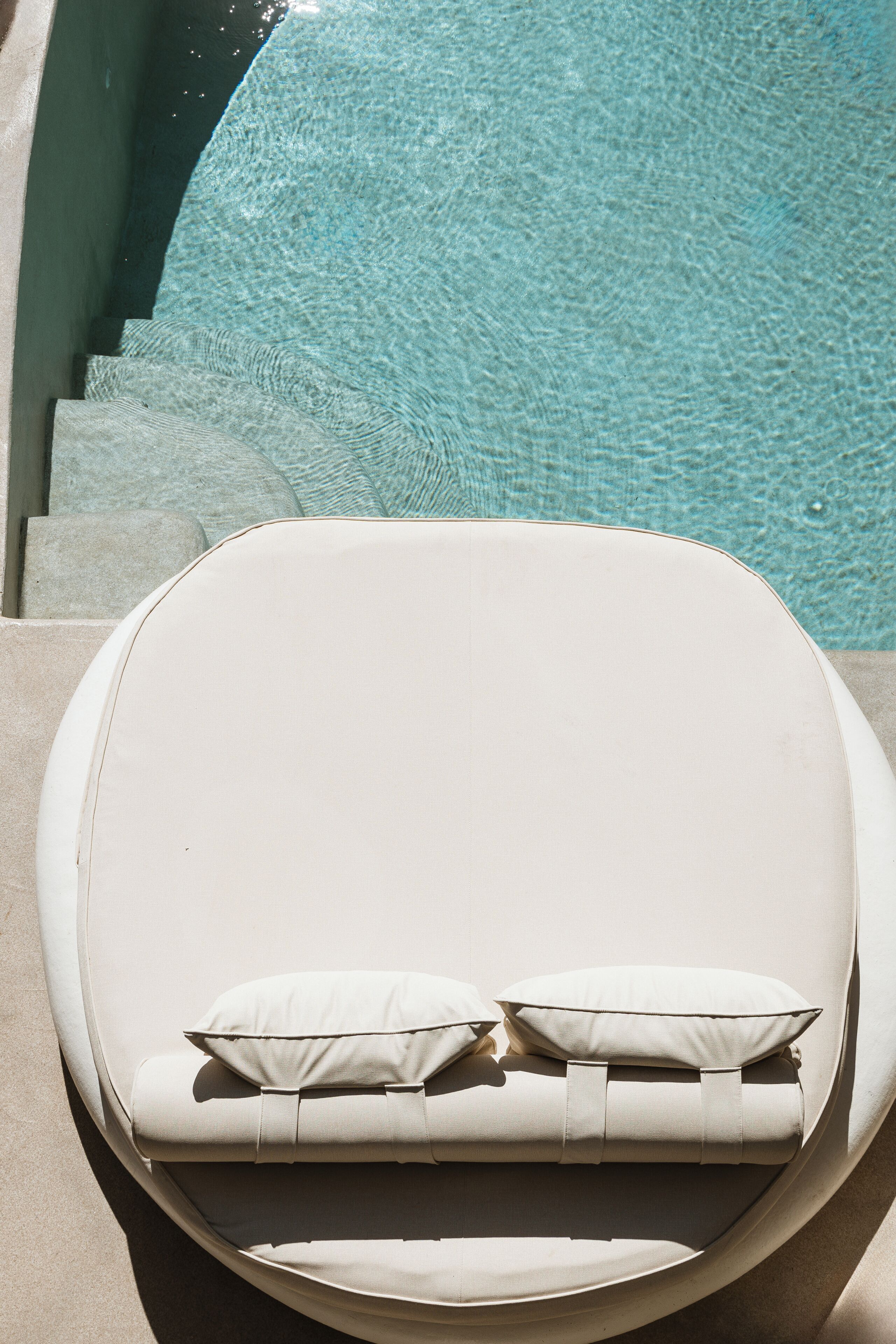 A sun lounger with cushions by a poolside.