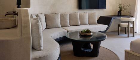 A modern living room with a curved sofa, a glass coffee table, and a flat-screen TV mounted on the wall.