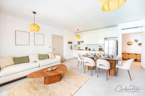 A modern living room with a sofa, coffee table, and dining area with chairs and a wooden table. - Dominicus Deluxe Apartment mit Poolblick (Dominicus)