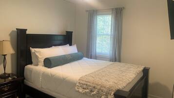 A neatly made bed with a headboard, a bedside lamp, and a window with curtains.