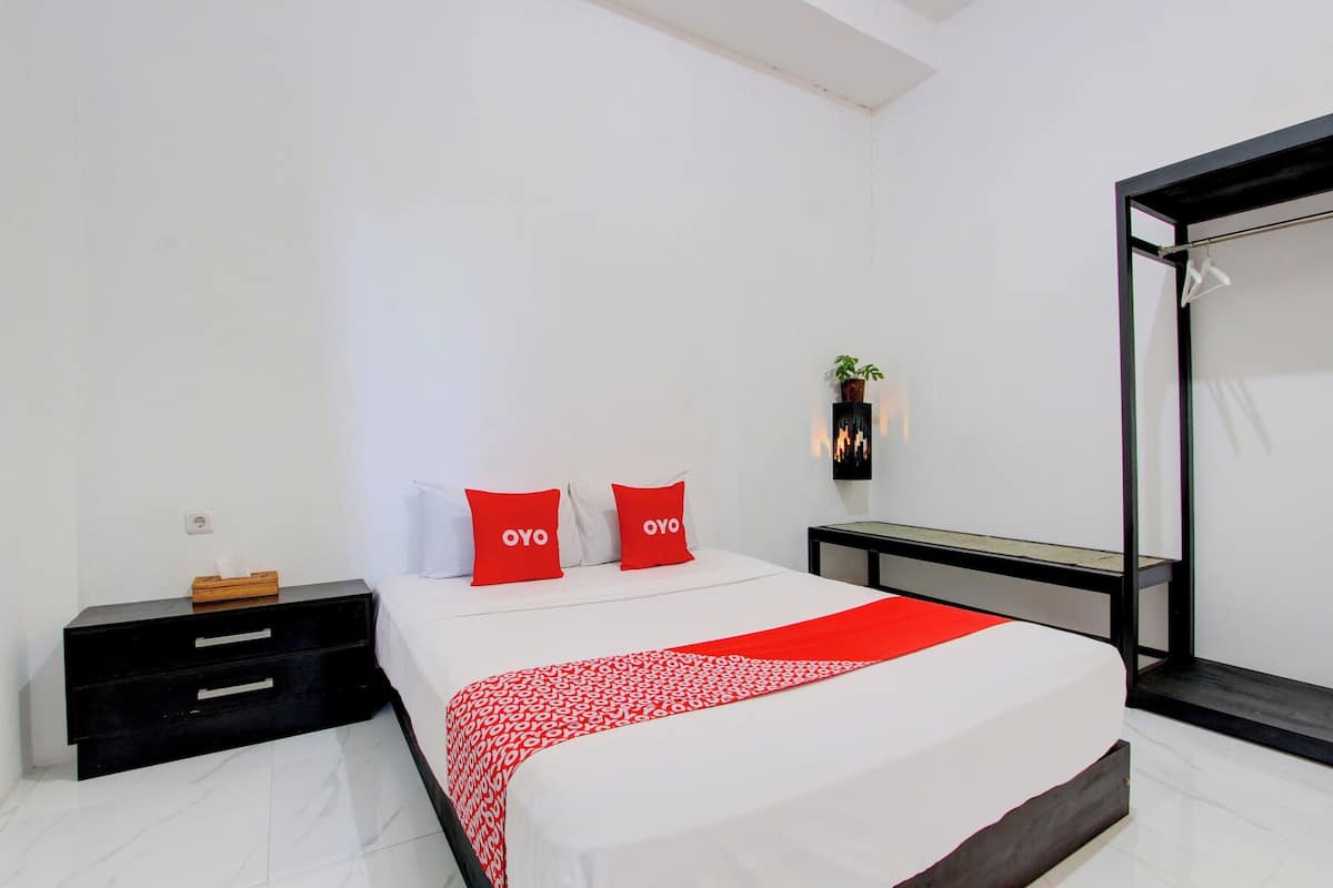 Ein modernes Hotelzimmer mit einem großen Bett, zwei roten Kissen, einem Nachttisch mit Taschentuchbox und einem schwarzen Beistelltisch.