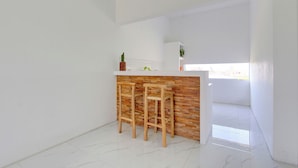 Eine Küche mit weißer Arbeitsplatte, Holzstühlen und einer Wand in Backsteinoptik.