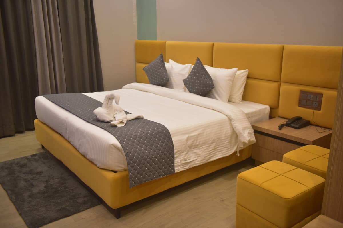 Una habitación de hotel con una cama grande, una mesita de noche con un teléfono y un pequeño otoman amarillo.