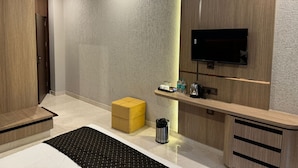 Un baño moderno con tocador de madera, lavabo negro, otoman amarillo y televisor montado.