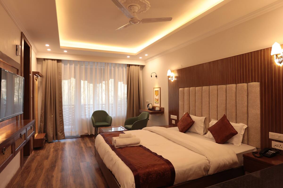 Una habitación de hotel con una cama grande, un escritorio con teléfono, una silla, un televisor y un ventilador de techo.