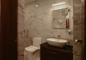 Une salle de bain avec un mur en marbre, un lavabo blanc, un miroir et des toilettes.