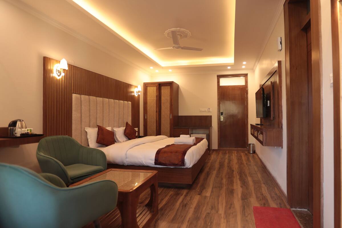 Habitación de hotel con dos camas, una zona de estar con una silla y una mesa, un televisor montado en la pared y un ventilador de techo.