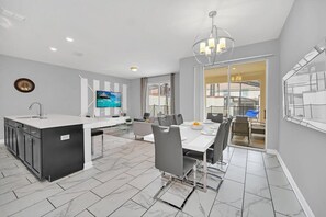 Una cocina moderna con una isla central, un comedor con una mesa grande y sillas, y un televisor montado en la pared.