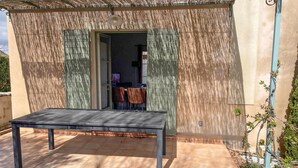An outdoor patio with a table and chairs, a covered area with a door, and a small garden with plants. - Awesome home in Saint-Rémy-de-Provence (Saint-Rémy-de-Provence)