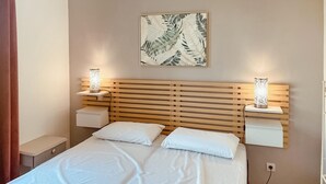 A bedroom with a wooden slatted headboard, two bedside tables with lamps, a bed with white linens, and a wall-mounted artwork of leaves. - Awesome home in Saint-Rémy-de-Provence (Saint-Rémy-de-Provence)