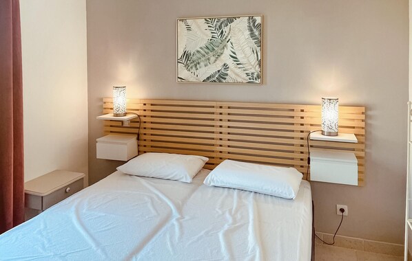 A bedroom with a wooden slatted headboard, two bedside tables with lamps, a bed with white linens, and a wall-mounted artwork of leaves. - Awesome home in Saint-Rémy-de-Provence (Saint-Rémy-de-Provence)